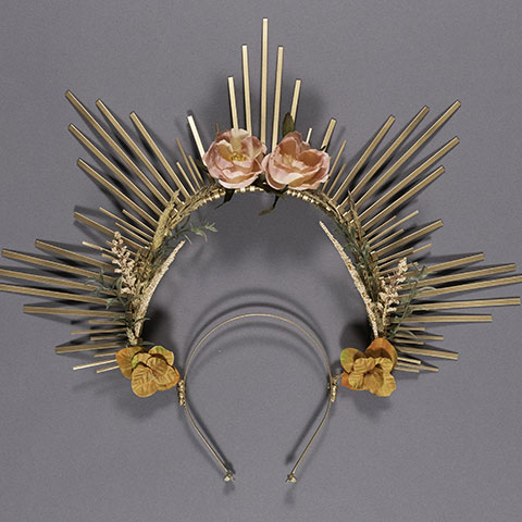 photo of a sculptured gold headpiece with long radiating tines, roses and leaves