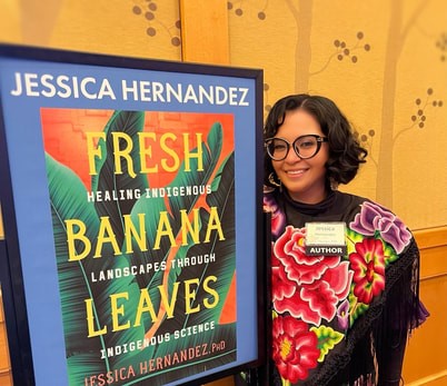 Dr. Jessica Hernandez stands next to a poster of her book