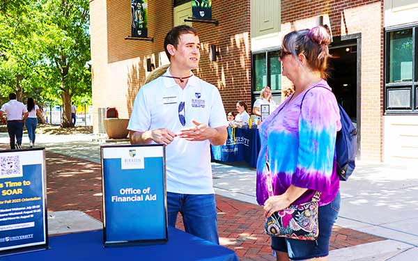 an Admissions staff member talks to the parent of a prospective student at an outdoor Admissions event on Boettcher Commons on campus