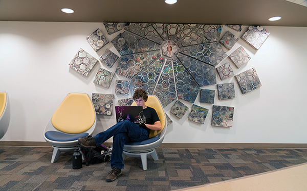 A student sits in an on-campus study space working hard on his laptop