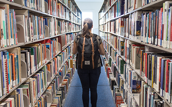 student walking between bookshelves