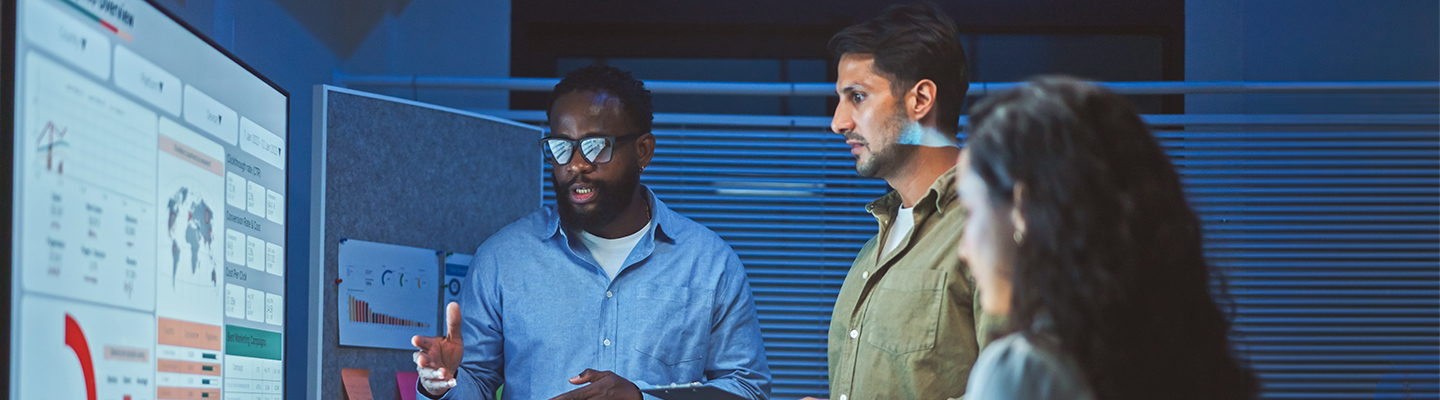 tech professionals look at a large screen full of charts and tables while they develop new Artificial Intelligence AI technologies