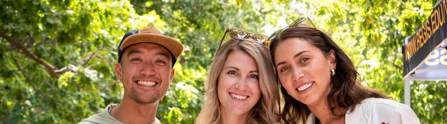 Three people pose together on the Regis campus