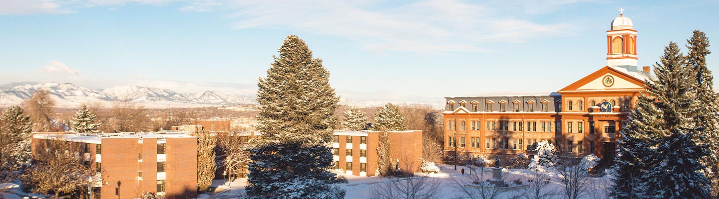 Aerial view of the northwest Denver campus covered in snow with snow-topped mountains in the background