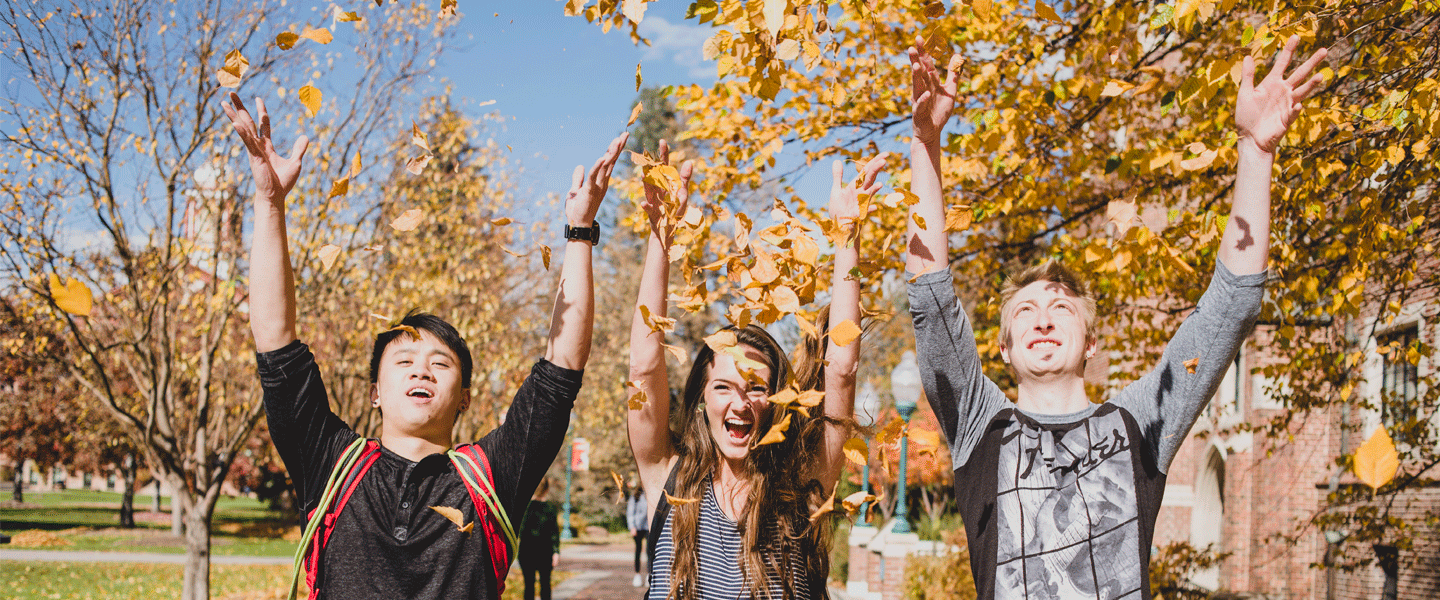 smiling students throwing leaves in air in fall