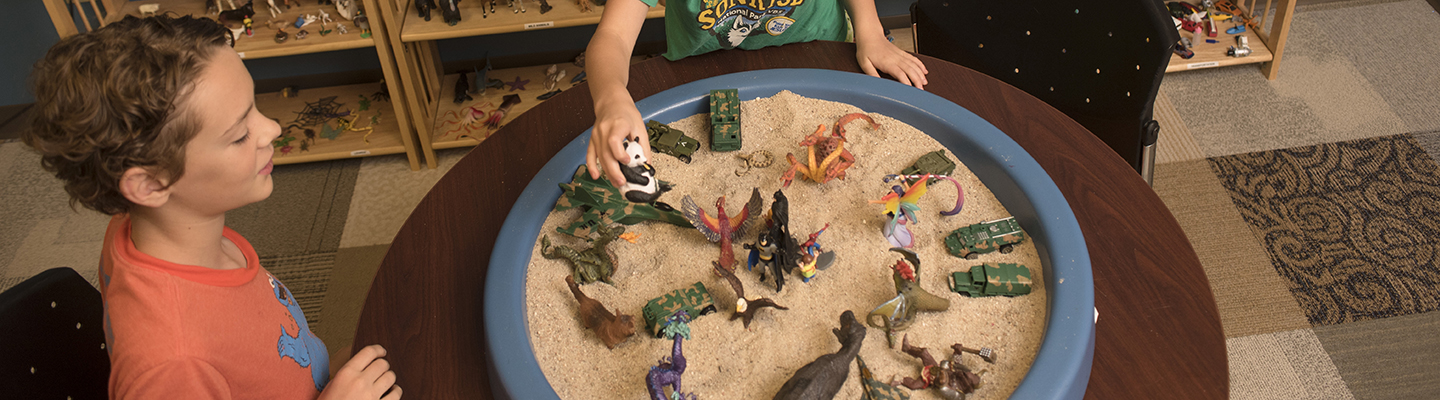 two children using sand and toys during therapy