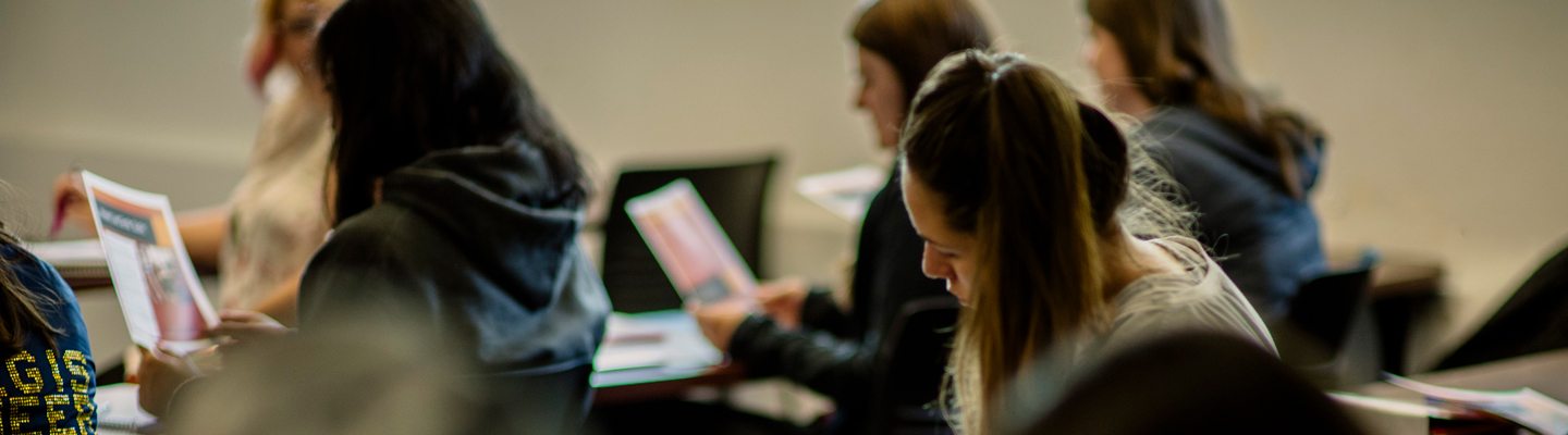 Students seated in a classroom, attentively reading and holding papers