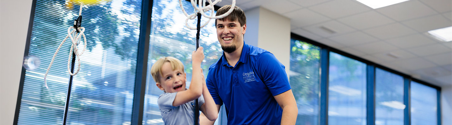 an Regis-Creighton Occupational Therapy student swings a young child on a swing during class