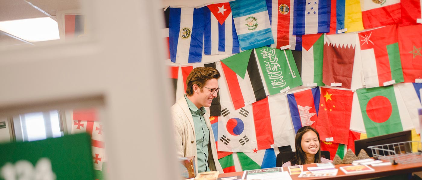 two people smile with international flags behind them