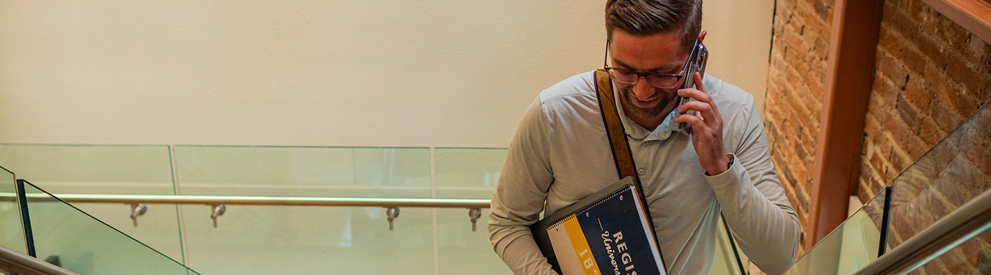 man climbs stairs carrying a Regis notebook and talking on a phone