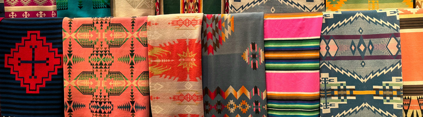 Row of colorful Native American blankets with geometric patterns hanging side-by-side.