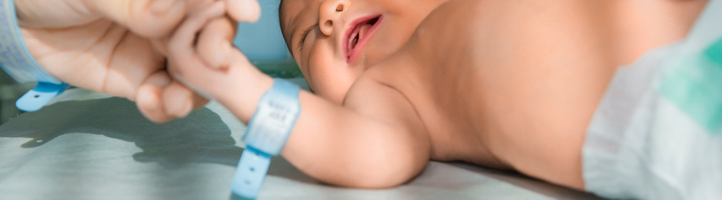 Adult holds hand with newborn baby in diaper