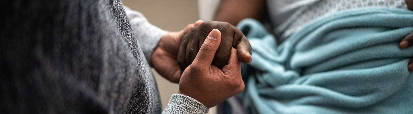 a caregiver holds the hand of a patient wearing hospital pajamas