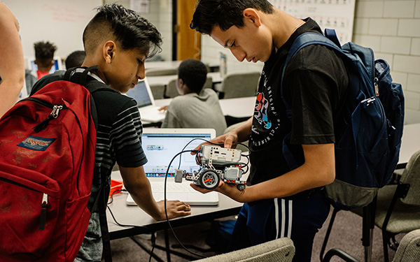 students in classroom work on computer and small robot