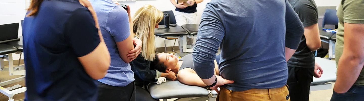 physical therapy professor demonstrates technique on a student in the physical therapy lab while other students observe