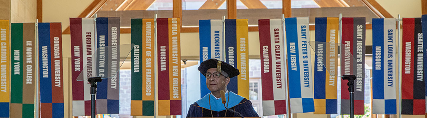 President Aceves stands behind a podium wearing regalia and speaking to the audience at his inauguration in the Chapel