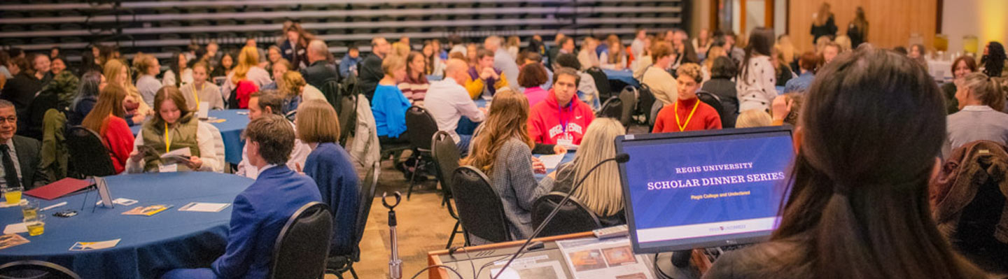 Parent and student sit at a table reading booklet while surrounded by people at their table and other tables in Mountain View Room