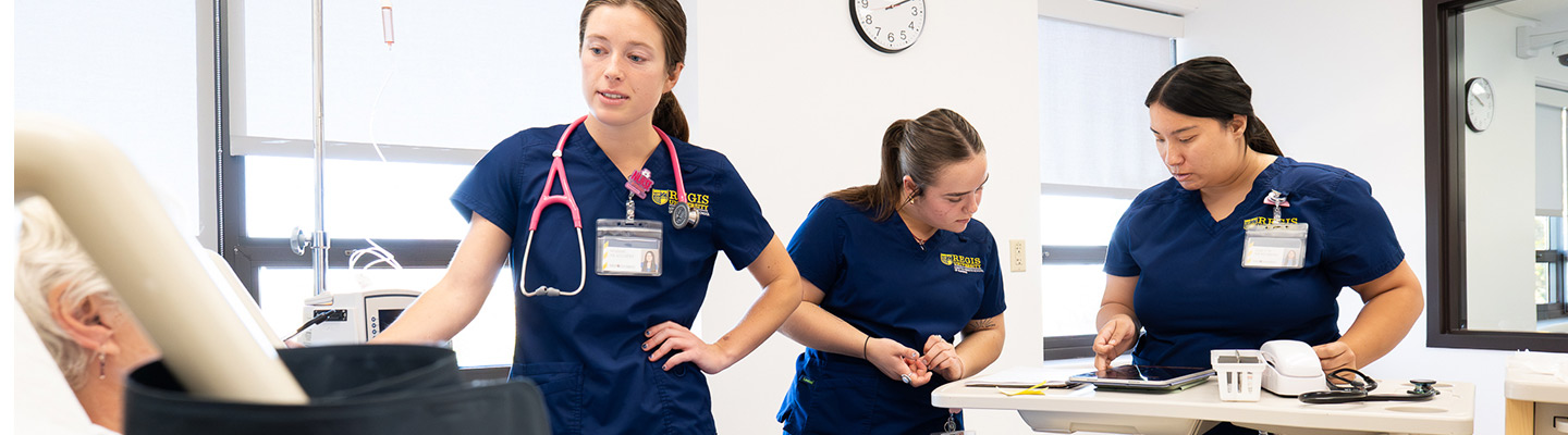 three Regis University students wearing scrubs work together to help a patient at the Clinical Simulation Laboratory at the Interprofessional Health Site in Thornton, Colorado