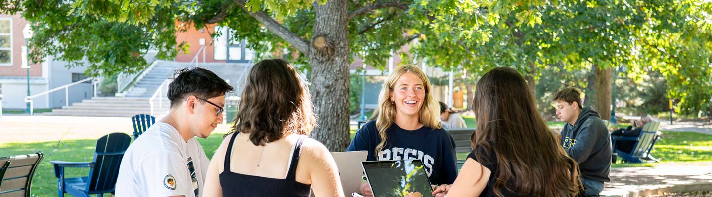 Students sit outside. A students sits and looks over to the right at another student