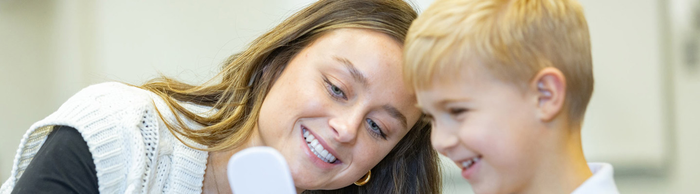 Teacher on the left smiling and holding a tool to a child to the right