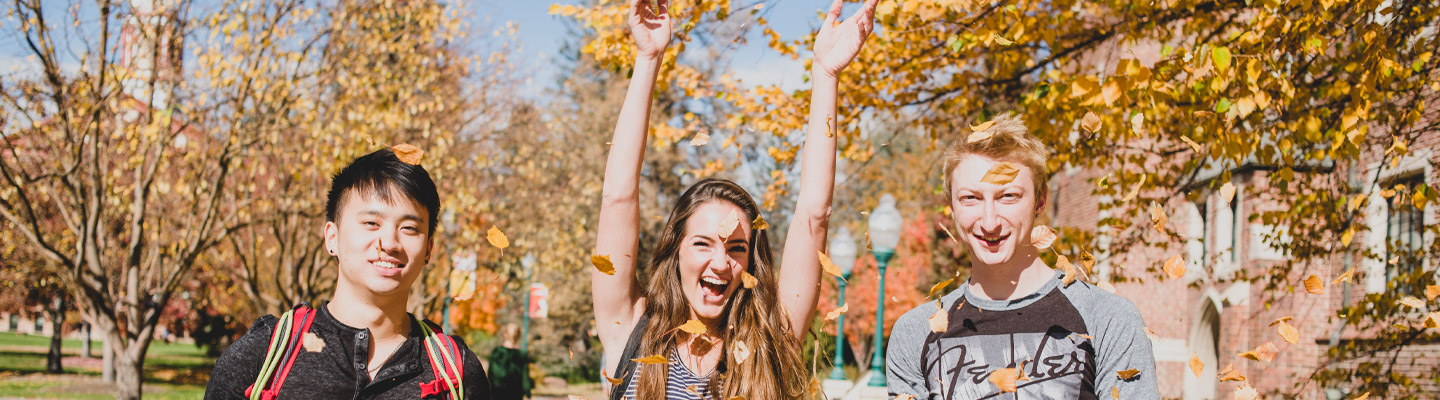 three students throwing leaves on campus in fall