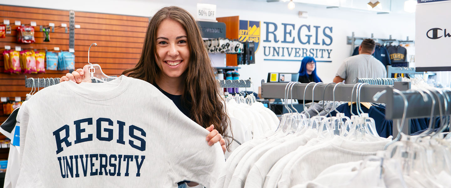 a student holds up a Regis sweatshirt in the Ranger Station bookstore on the Northwest Denver Campus