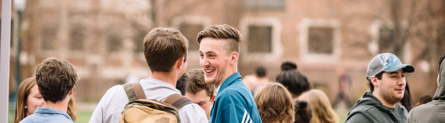In the middle, two students look at each other smiling. Multiple students stand beside them on the left and the right.
