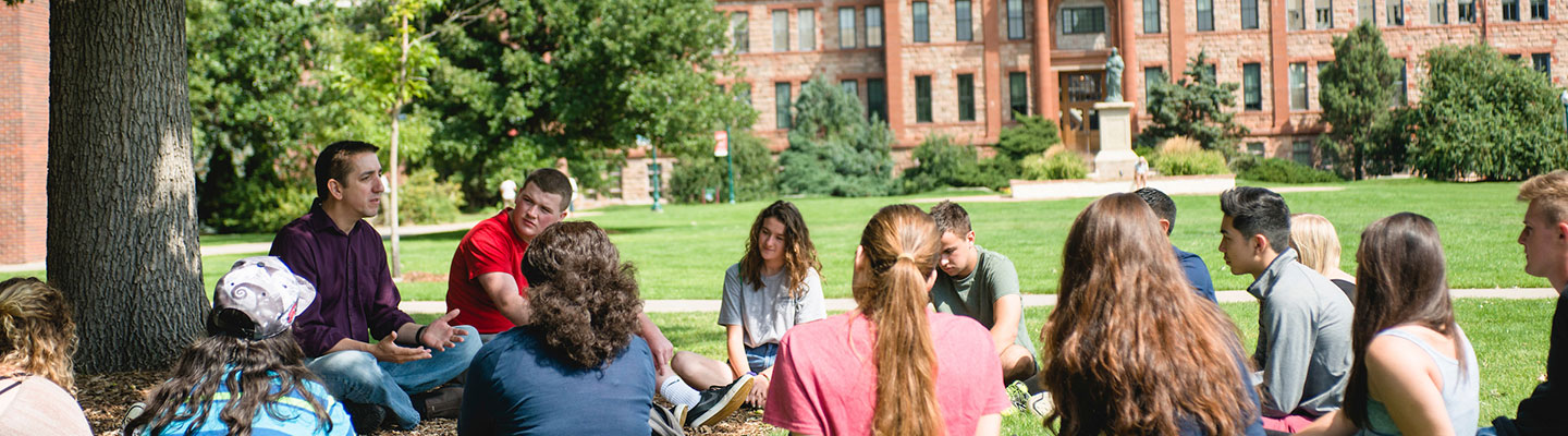 students and an instructor sit on the grass in the Quad while having an academic conversation
