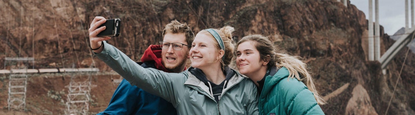 three students pose for a group selfie on an Outdoor Adventure Program trip to the Hoover Dam