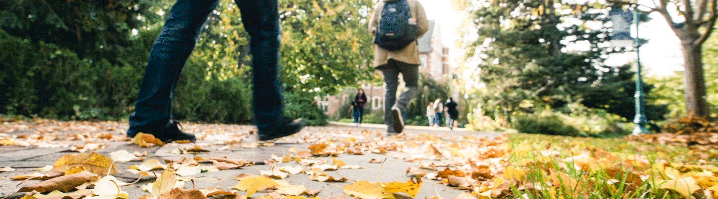 two students feet walking on fall leaves