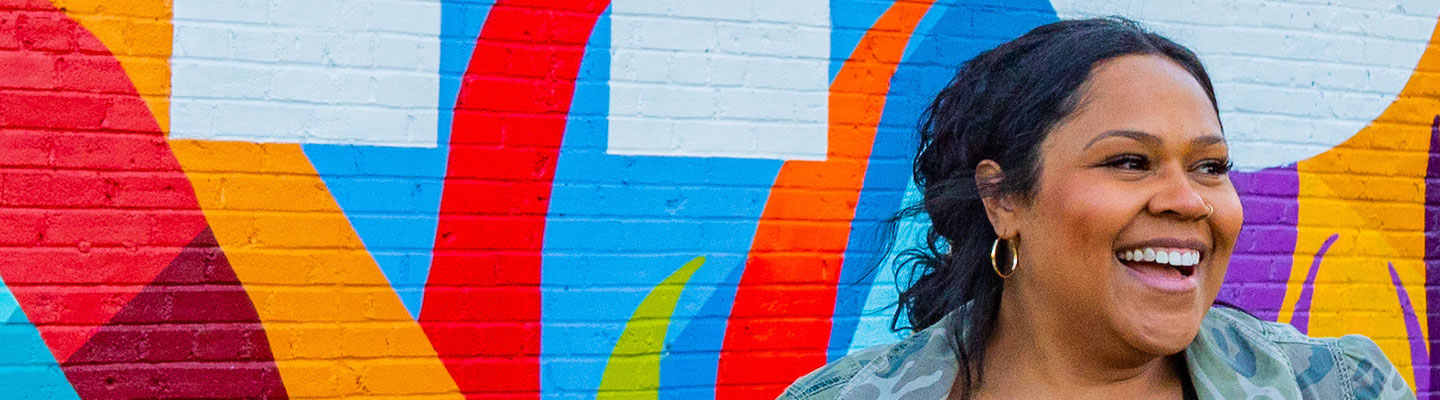woman smiles in front of colorful abstract mural