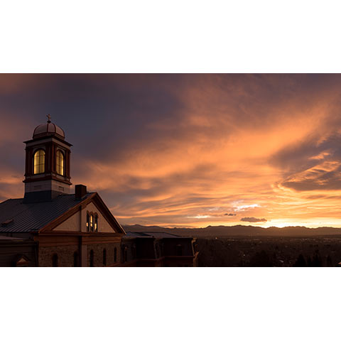 a photo of the top of main hall during a dramatic, colorful sunset with sweeping clouds and the Rocky Mountains in the background