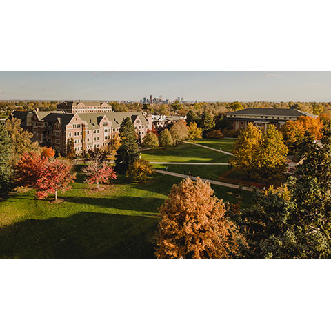 A view across the Quad with the library, Carroll Hall, Felix Pomponio Science Center and David Clark Hall in the foreground and the denver skyline in the background 