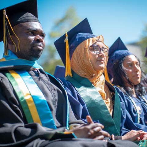 Regis University graduates seated in caps and gowns during an outdoor commencement ceremony