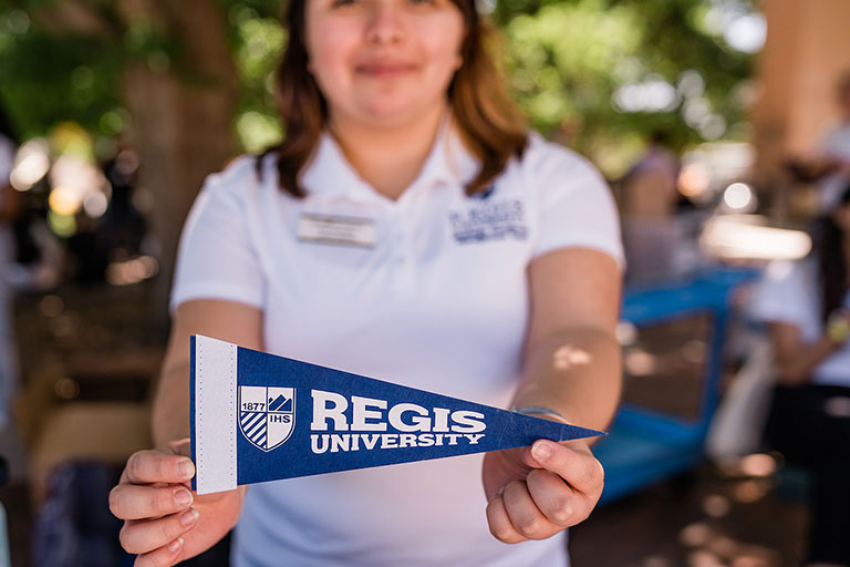 staff member wearing a Regis polo shirt holds up a Regis pennant flag