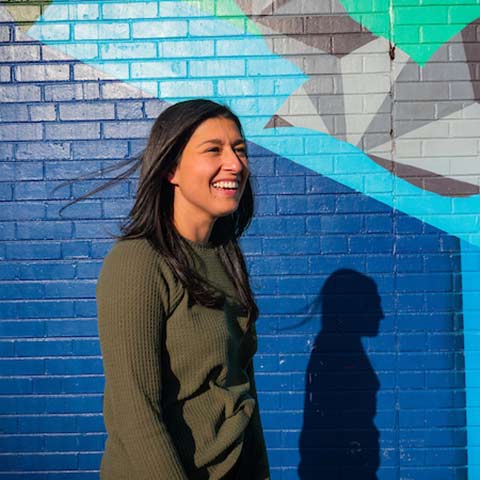 young woman smiles while standing in front of a colorful mural