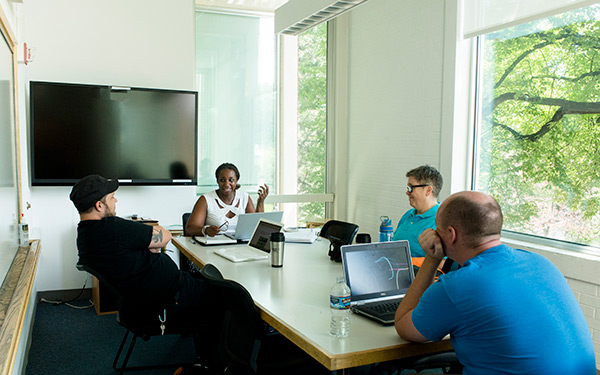 a group of adult students sits around a conference table talking and working on laptops