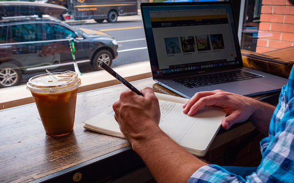 man writing in a notebook while seated at a coffee shop