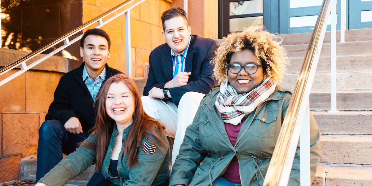 four adult students sit on the steps of main hall together smiling