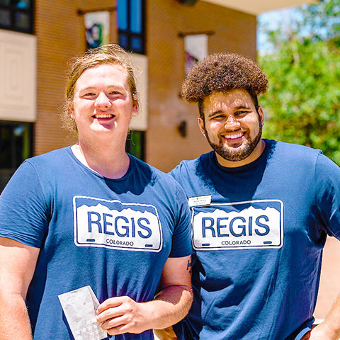 two students smile during an event on the quad on the Regis campus