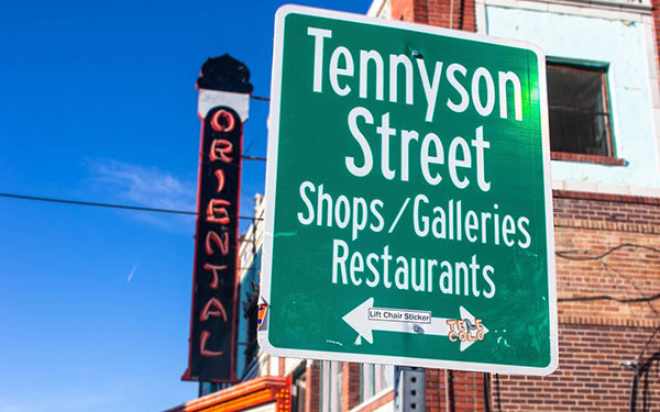 A street sign reading "Tennyson Street, Shops/Galleries, Restaraunts" stands in front of the neon sign for the Oriental Theater on Tennyson Street in the Berkeley Neighborhhod