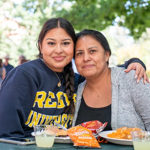 Regis University student and family member sitting together at an outdoor campus gathering