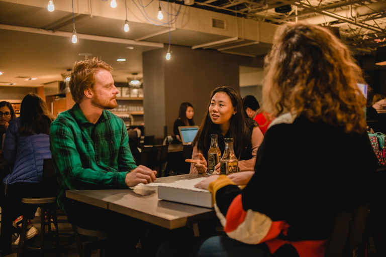 Three students gathered around a table chatting over dinner and drinks