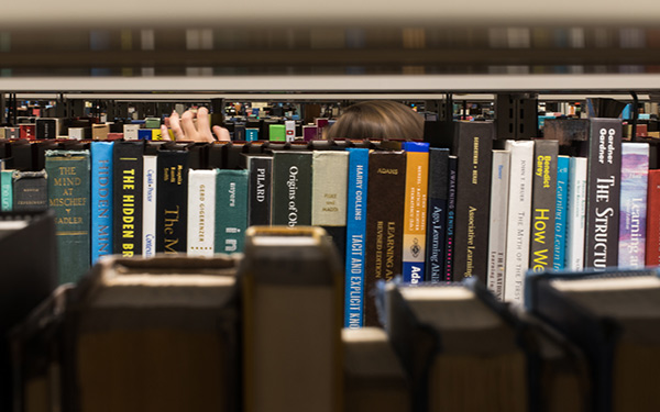a hand searches books on a shelf