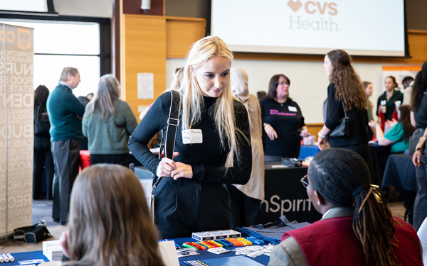 Student speaking with a CVS Health recruiter at a career fair table, with other booths and attendees in the background.