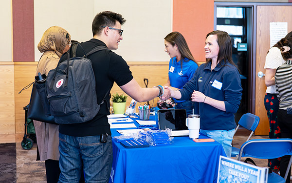 a student shakes hand with a potential employer across a table littered with brochures during a career fair on the Regis campus