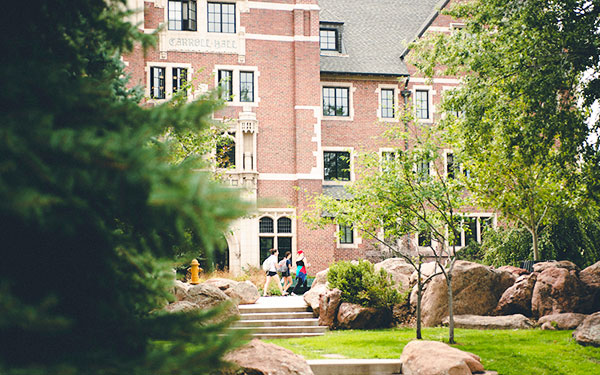 a view through the trees as students walk past a historic red brick building on the beautiful Denver, Colorado campus