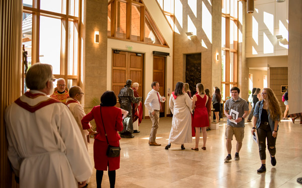 Students, faculty and community members gather in a sunlit chapel at Regis University, dressed in formal and liturgical attire