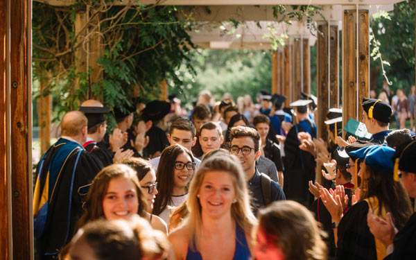 Students walking through a line of faculty in academic regalia during a campus ceremony.