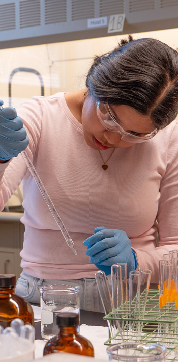 Regis University student conducting a lab experiment using a pipette and test tubes